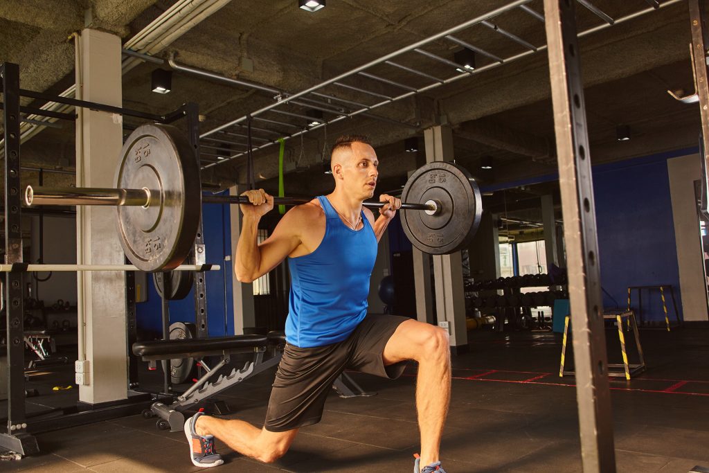 Young male fitness model training squat with weight at the gym