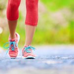 Jogging woman with athletic legs and running shoes. Female walking on trail in forest in healthy lifestyle concept with close up on running shoes. Female athlete jogger training outdoors.