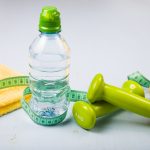 Dumbbells, an apple, a towel and a bottle of water on a blue wooden table. Concept of fitness and a healthy lifestyle.