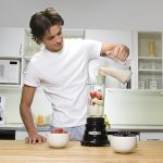 Young man in kitchen, pouring milk into blender