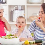 Happy young family preparing and eating vegetable salad
