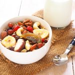 Close up of a healthy bowl of muesli mixed with dried fruit and nuts and almond milk on a wooden background.