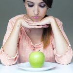 Upset brunette woman with green apple on a plate.