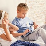 Technology for home use. Little girl listening to music on headphones and cute small boy enjoying his digital tablet in room